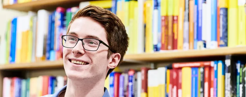 A maths student smiling and sitting in front of a book shelf.