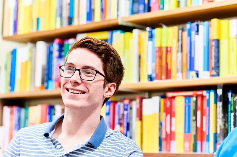 Student in front of a bookshelf, smiling a the camera.