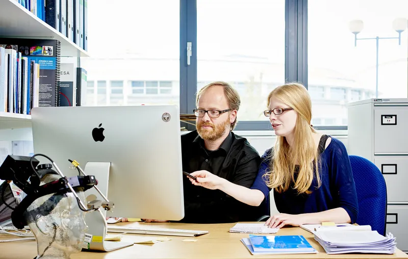 Two members of staff discussion data displayed on a desktop computer