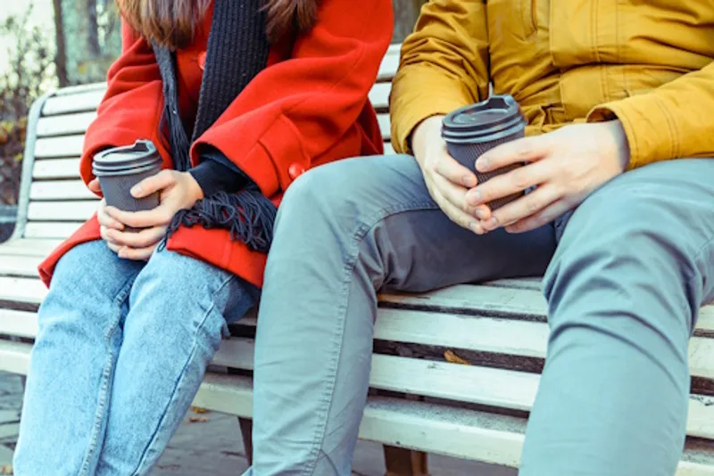 Two people sitting on a bench drinking coffee from paper cups