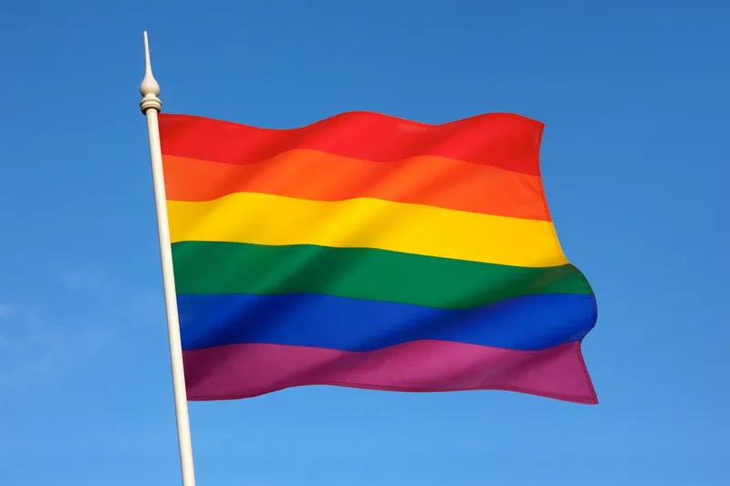 Image of the LGBT+ flag with blue sky background