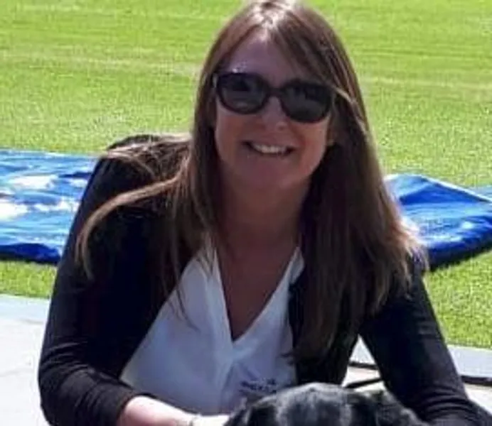 Headshot of Angela Johnson, she is light skinned, wearing sunglasses and a dark cardigan, and is with her guide dog Nutmeg, a black Labrador.