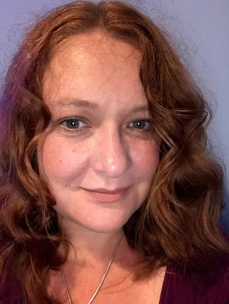 Headshot of Siobhan Kennedy who is light skinned and has dark red wavy hair