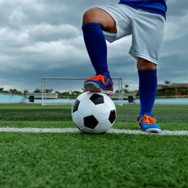 Footballer from the waist down with their foot on a football on a grass pitch