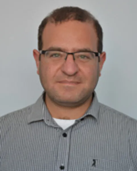 Headshot style photograph of Dr Iddo Amit, BSc MSc PhD MIEEE MInstP FHEA in front of a grey background