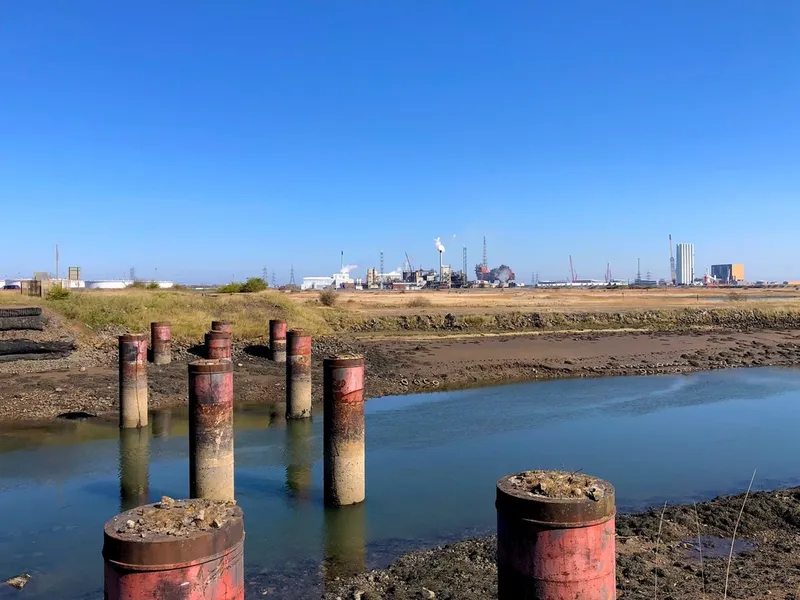 Industrial works on a river with blue sky above.