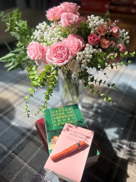 Flowers in a vase, books & pen on a table.