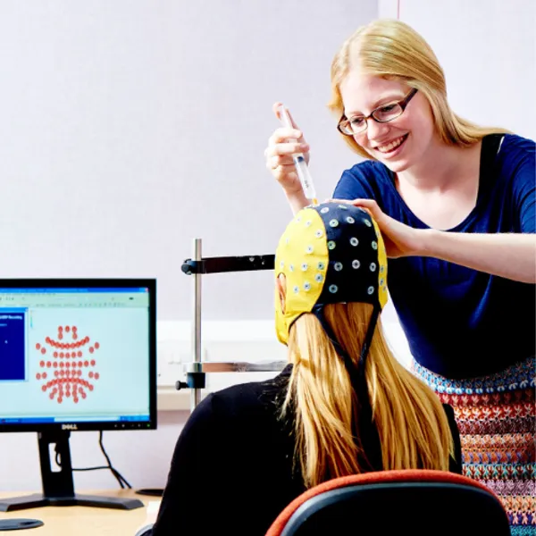 A researcher injecting fluid into a cap worn by a student