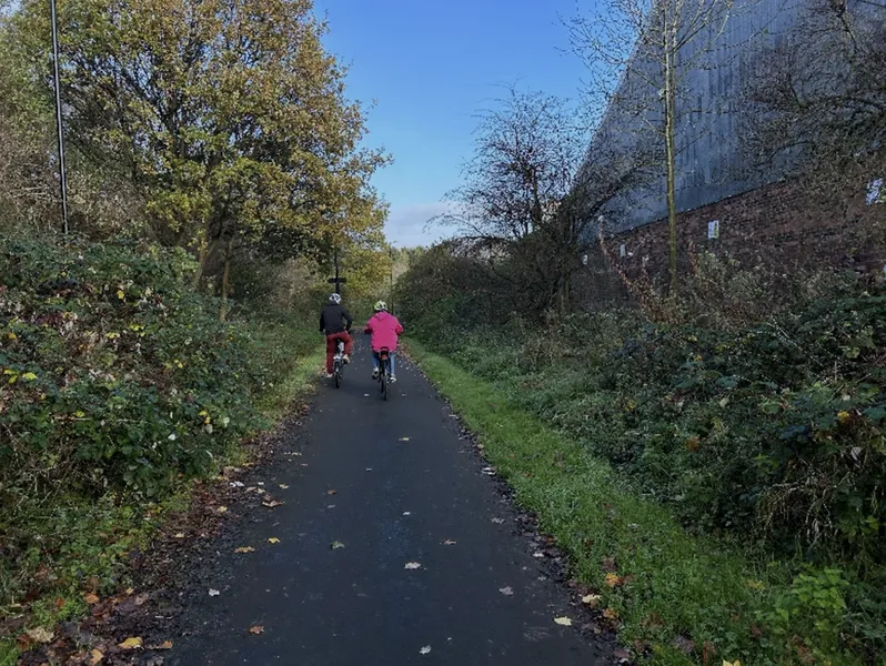 Photograph of two cyclists cycling away from the camera, down a nature path with trees surrounding it.