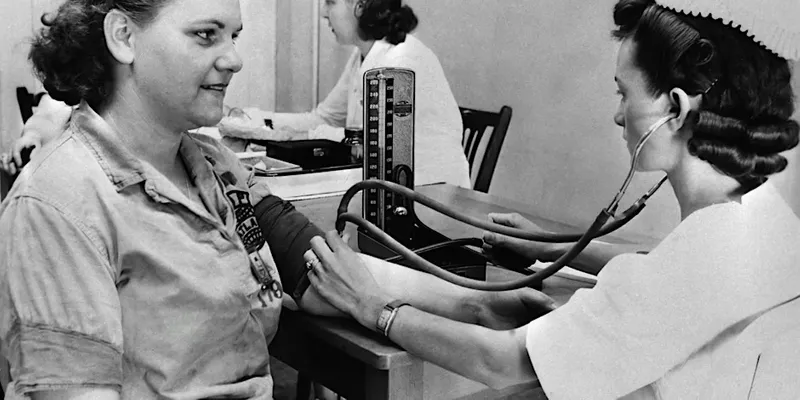 (black and white) A nurse in a uniform checks a woman's blood pressure using a sphygmomanometer and stethoscope in a clinical setting