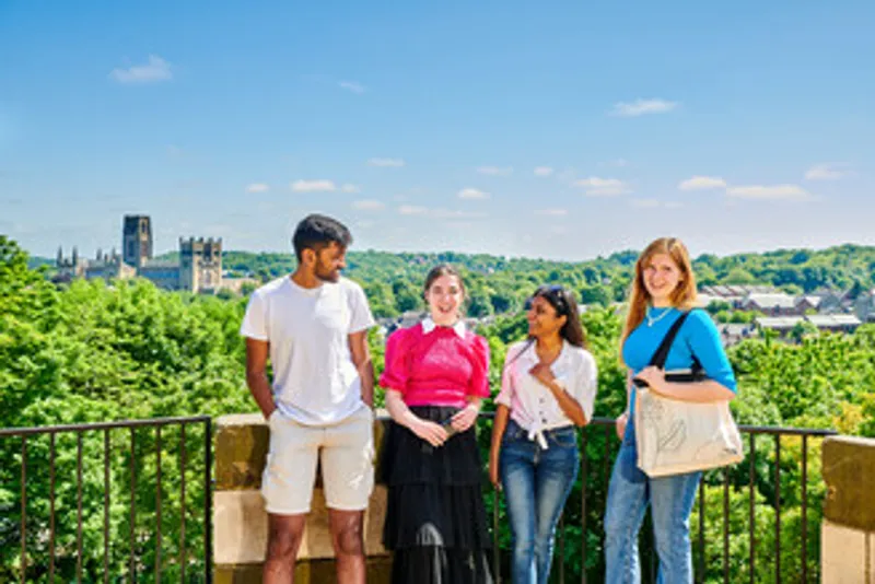 Four students dressed in casual summer clothes stand against some railings - the cathedral and bright green tree tops can be seen behind them