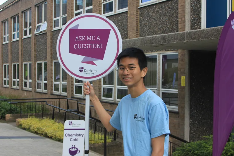 Image of a student ambassador holding an ask me sign during an open day