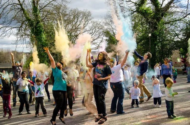 Crowd of people taking part in the powder throw at Holi Festival. The people are jumping in the air and are covered in coloured powder.