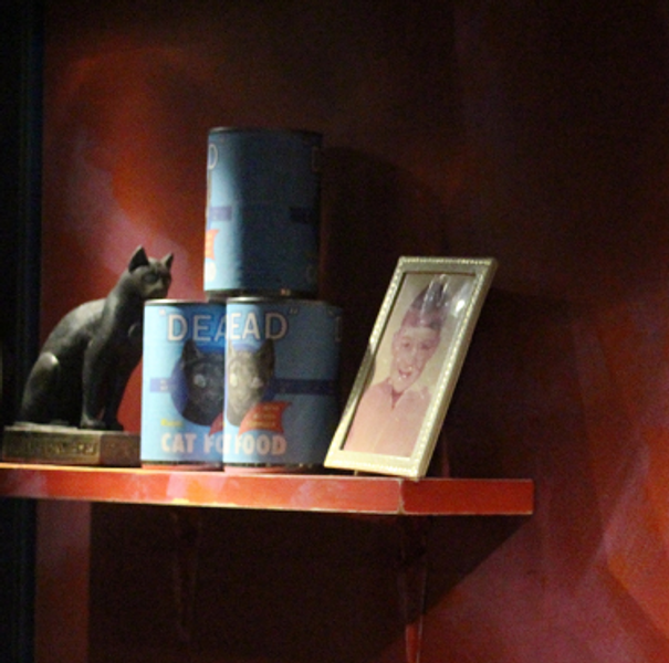 Part of art installation including an ancient Egyptian cat model, modern cat food tins, a photograph and the painted words ‘dust to dust’ on the background.
