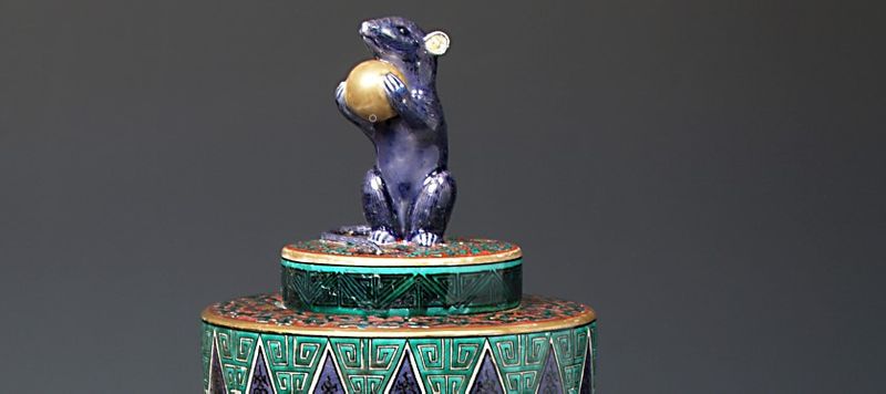 Ornament depicting a rat holding a ball and stood on a platform