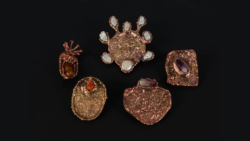 Group of five brooches made from a copper-coloured metal in different shapes with stones set into them.