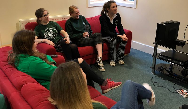 Students watching a flat-screen TV mounted on a wall, sitting on couches in the Junior Common Room at Parson's Field site.