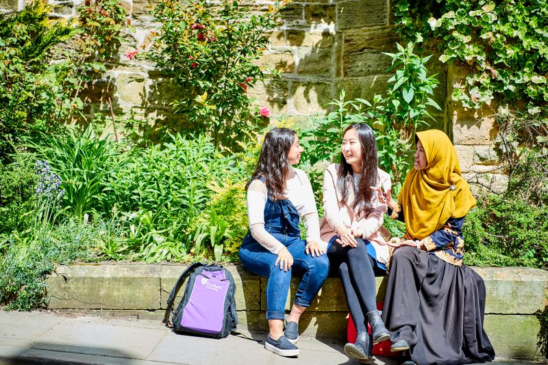 3 female students sitting on a wall chatting
