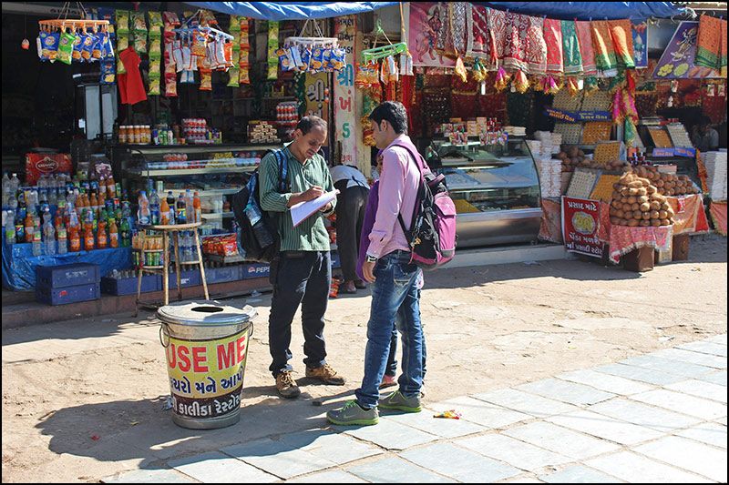 Photograph of two men talking in front of brightly coloured shops
