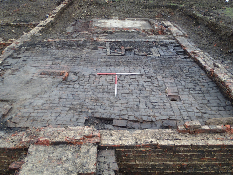 Excavated brick surface surrounded by brick walls and a red and white scale in the centre