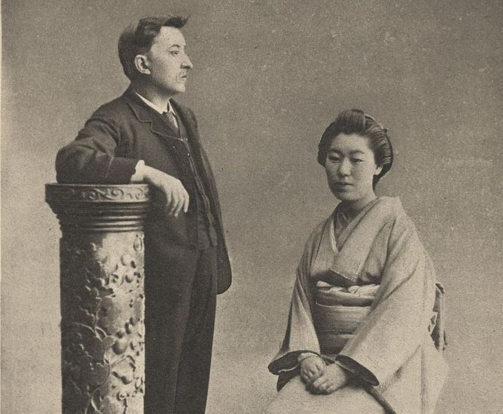 A man leaning against a pillar with his wife sitting next to him