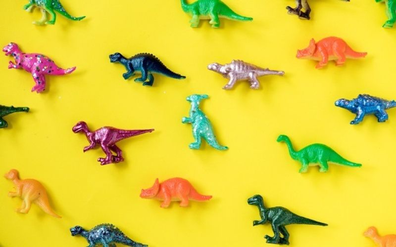 Group of different dinosaur toys laid out on a bright yellow background