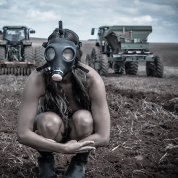 Woman crouched in gas mask with tank and tractor behind her