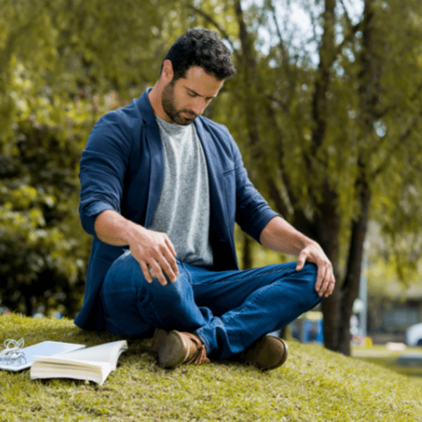 Man meditating in the park with a book by his side