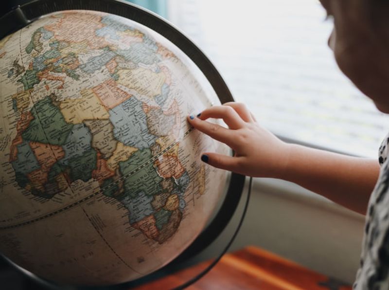 A hand pointing at a desk globe