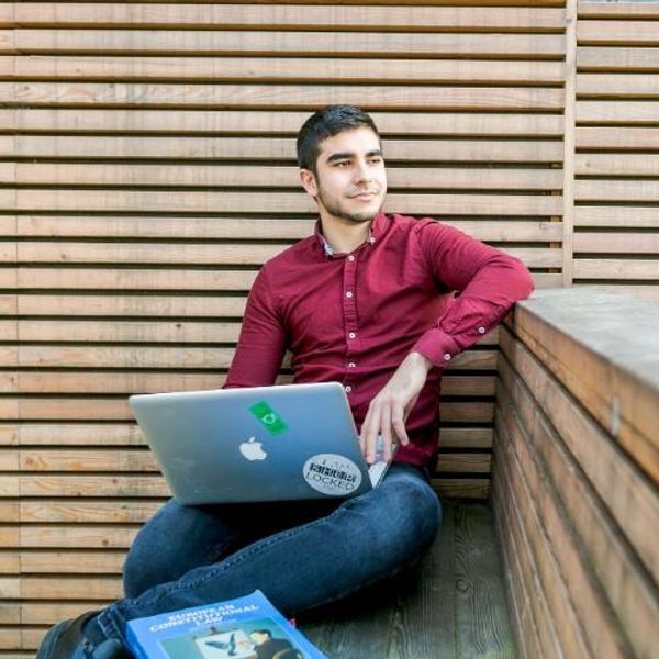 Student sitting by a wall with a laptop