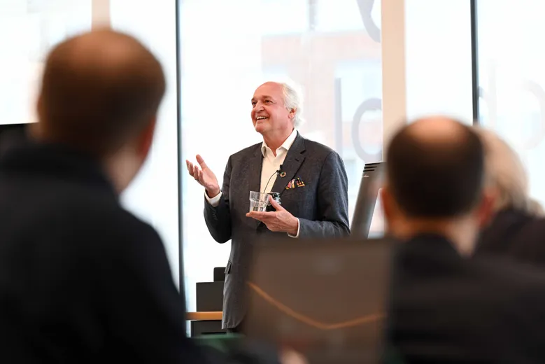 White haired man giving speech, backs of heads in front