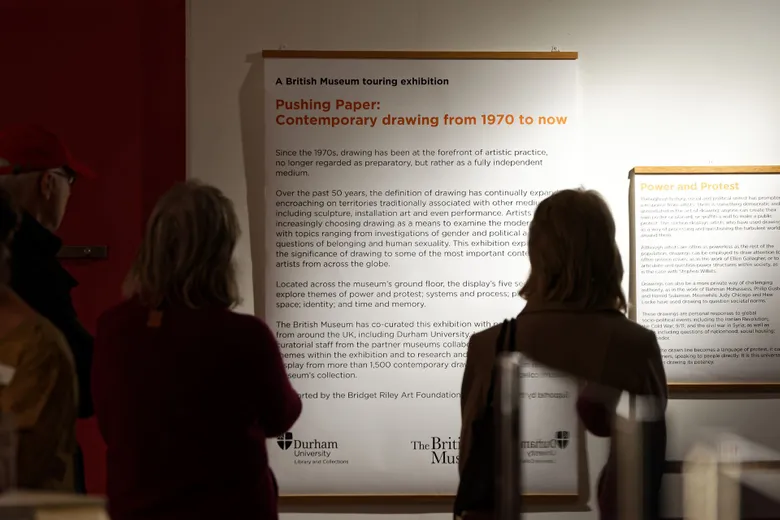 Two exhibition visitors reading the Pushing Paper exhibition information