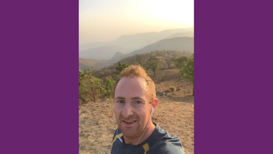 A red haired man in running gear taking a selfie with a range of hills behind him