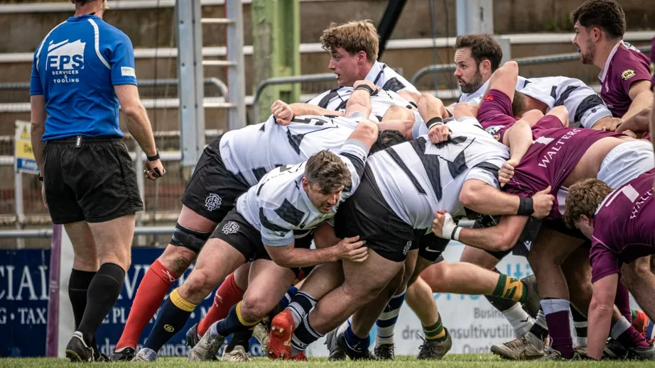 Two teams of rugby players wearing purple tops, and black and white tops, playing against each other