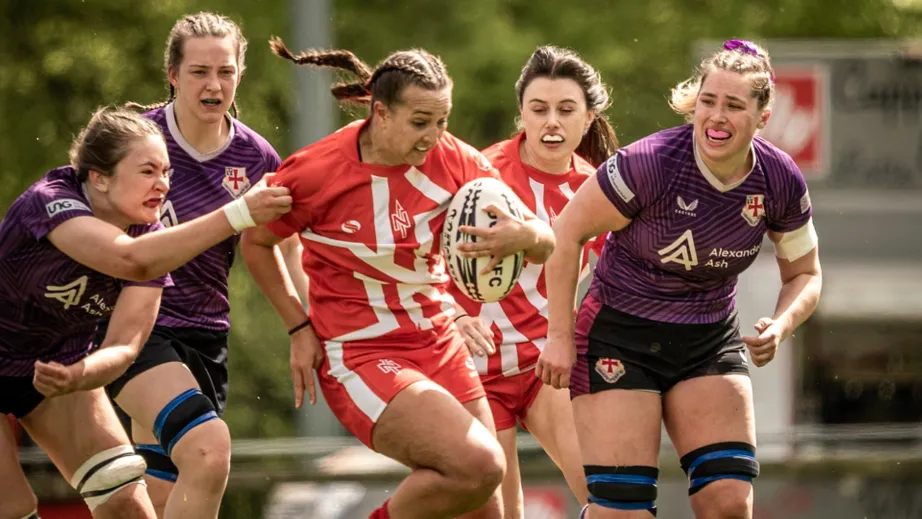 Two teams of female rugby players wearing purple tops, and red and white tops, playing against each other