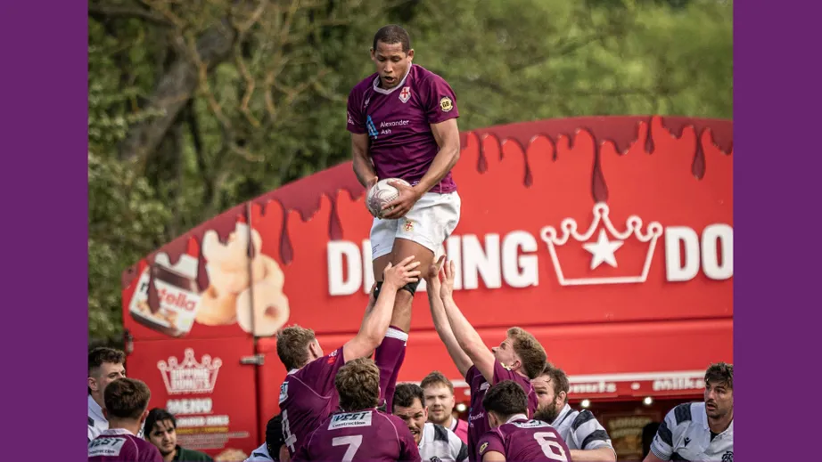 Two teams of rugby players wearing purple tops, and black and white tops, playing against each other