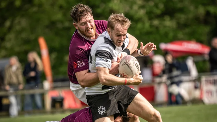 Two teams of rugby players wearing purple tops, and black and white tops, playing against each other