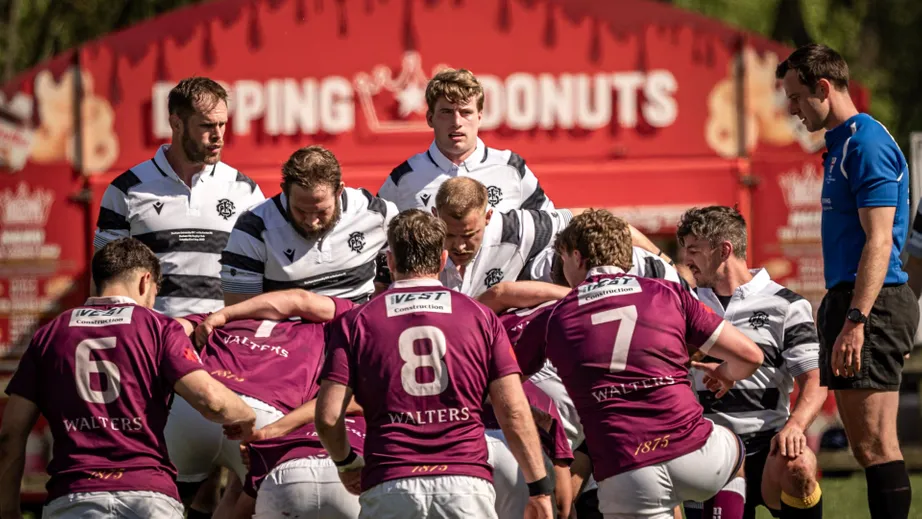 Two teams of rugby players wearing purple tops, and black and white tops, playing against each other