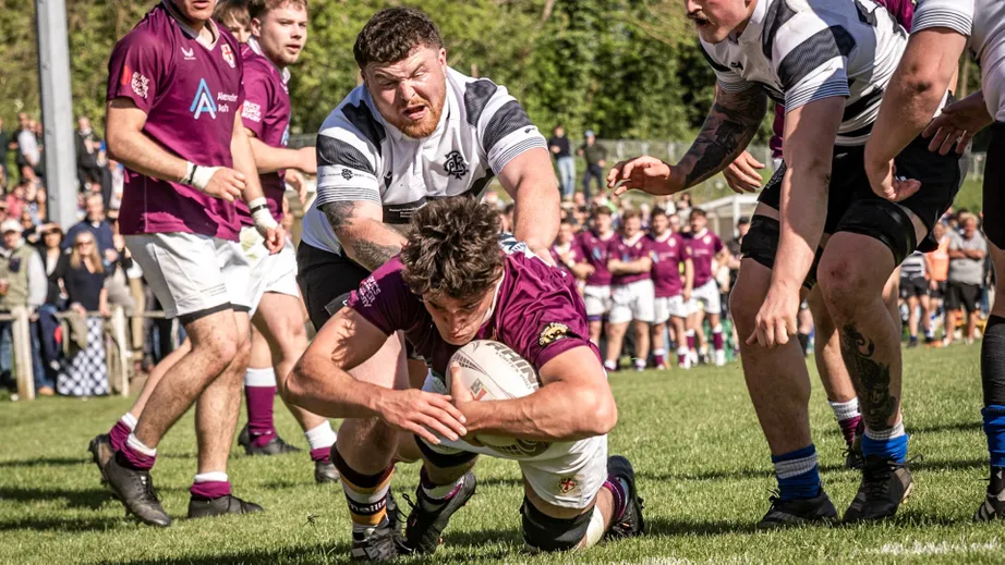 Two teams of rugby players wearing purple tops, and black and white tops, playing against each other