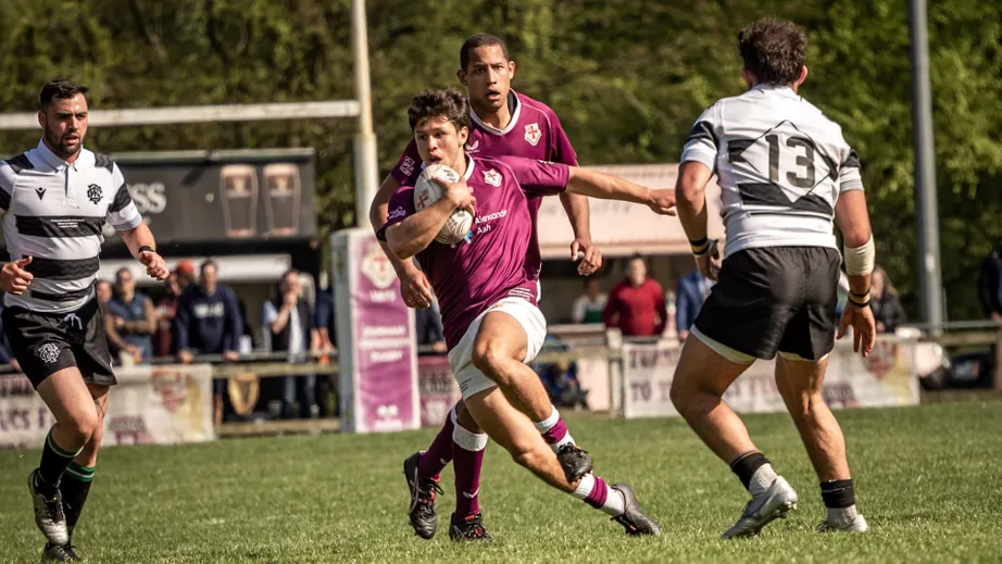 Two teams of rugby players wearing purple tops, and black and white tops, playing against each other