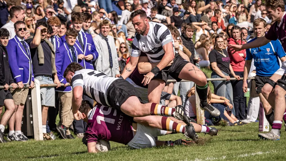 Two teams of rugby players wearing purple tops, and black and white tops, playing against each other