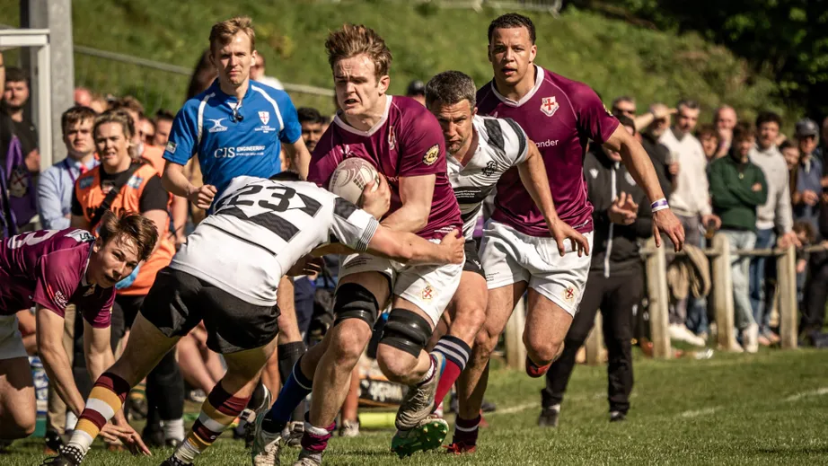 Two teams of rugby players wearing purple tops, and black and white tops, playing against each other