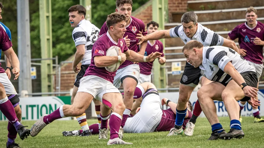 Two teams of rugby players wearing purple tops, and black and white tops, playing against each other