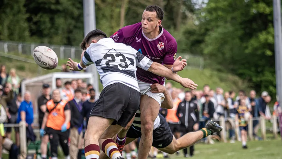 Two rugby players wearing purple tops, and black and white tops, playing against each other