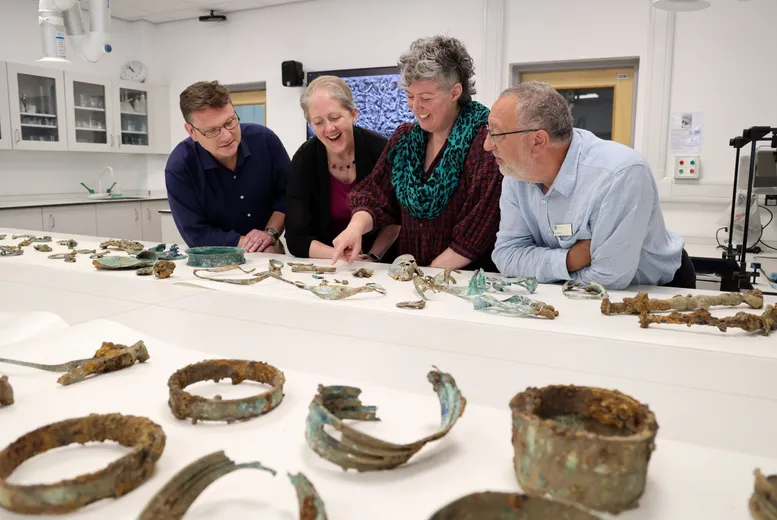 The Melsonby Hoard team stood talking to each other next to a white table where a number of Iron Age artefacts are laid out.