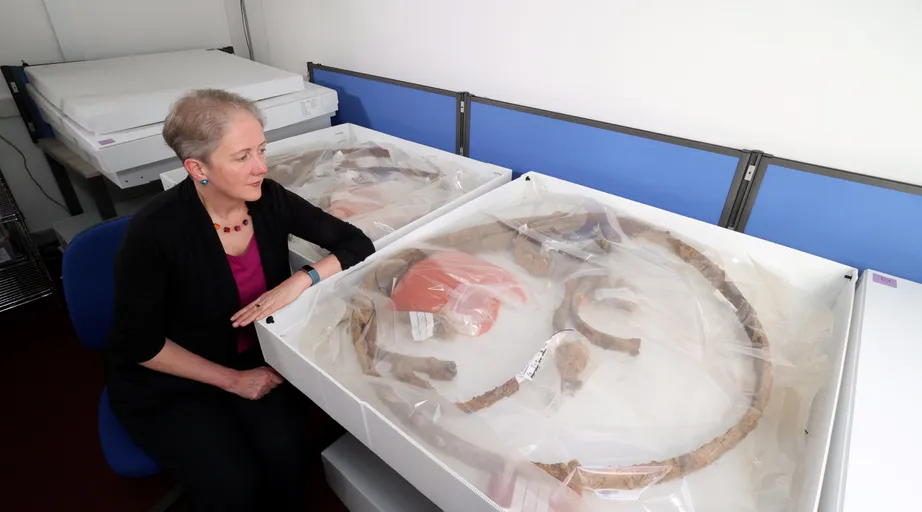 Dr Emily Williams sat next to a preserved iron tyre from a chariot or wagon, excavated from the Melsonby Hoard