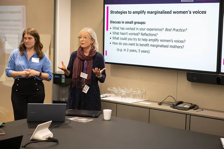 Two woman standing speaking, with a PowerPoint slide visible