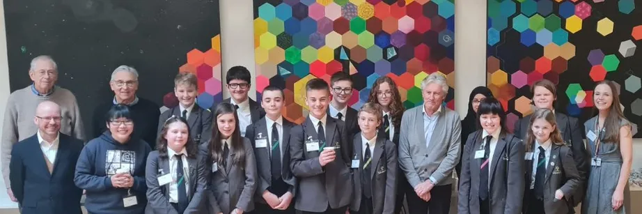 School pupils and guests smile for the camera in front of a large multi-coloured mosaic artwork