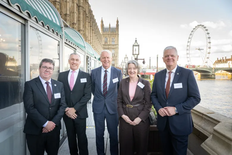 Four men and a woman standing outside Houses of Parliament, with London Eye in background