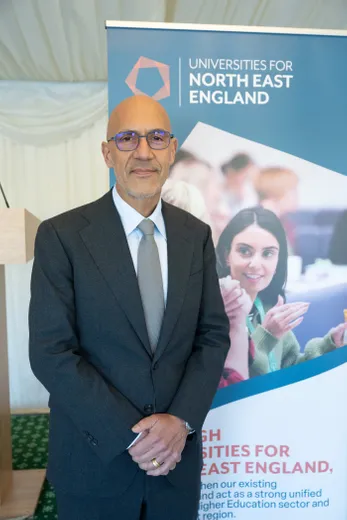 Man in suit standing in front of pull-up banner, looking at camera